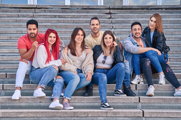 Obraz premium Group of friends smiling at the camera while sitting together on outdoor stairs. Friendship and positivity concept.