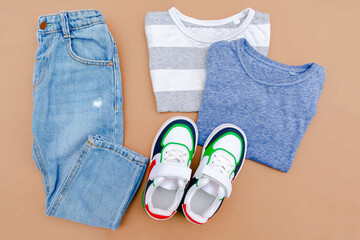 Baby sneakers,t shirt and jeans pants. Set of children's clothes and accessories for spring, autumn or summer. Fashion kids outfit,clothing on beige brown background. Flat lay, top view, overhead