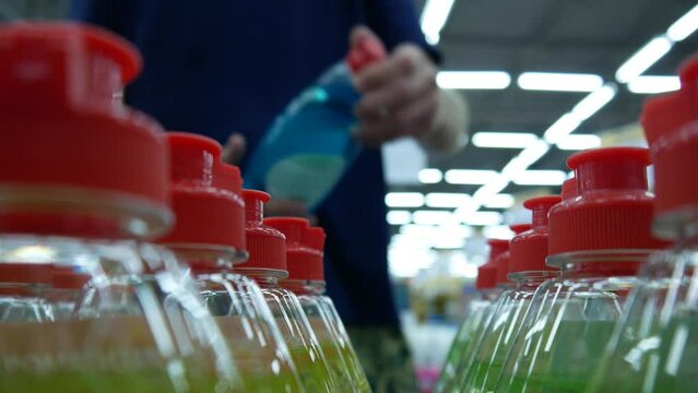 Close-up of many dishwashing liquid bottles with red caps on a store shelf and a man takes one