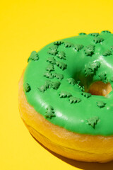 Green donut on a yellow background from the side, vertical photo. Studio shooting.
