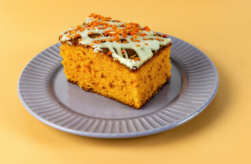 piece of carrot cake with white cream on a yellow background