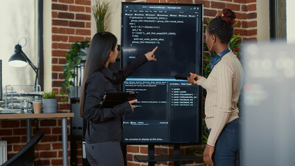 Team of programmers analyzing code on wall screen tv looking for bugs and errors while holding...