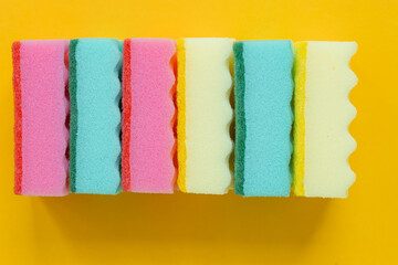 Plenty of bright multicolored sponges on yellow background, top view. Cleaning concept