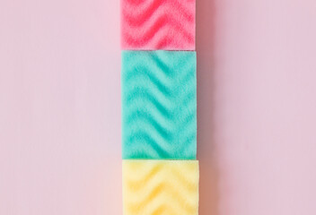 Fototapeta na wymiar Multicolored sponges for cleaning folded pyramid on a pink background.