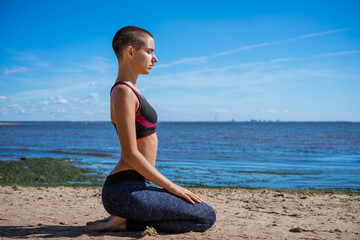 Fototapeta na wymiar Young slim woman doing yoga outdoors on sandy shore bay on sunny day. Unity with the concept of nature. Caucasian girl meditates and works on herself