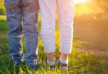 two pairs of children's legs in jeans close-up outdoors in the sun
