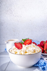 Bowl of homemade natural farm cottage cheese with fresh raw strawberry. Summer healthy diet balanced breakfast, morning snack, on white tiled background copy space