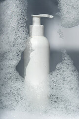 Fototapeta na wymiar A bottle of gel or shampoo on a background of white foam.