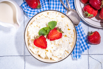 Bowl of homemade natural farm cottage cheese with fresh raw strawberry. Summer healthy diet balanced breakfast, morning snack, on white tiled background copy space