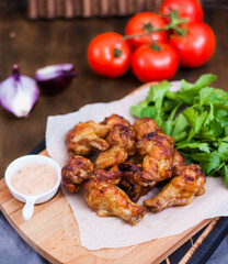 Spicy Homemade Buffalo wings with sauce, beer, tomatoes and herbs on a wooden board. Restaurant serving.