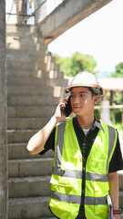 Young male inspector or architect in helmet and safety reflective vest standing with crossed arms at construction site