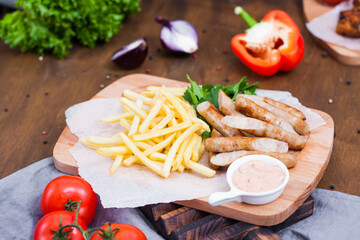 Fried sausages served on a board with French fries, sauce and herbs