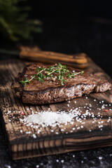 Beef tenderloin steak with salt and herbs on a wooden board on a dark background