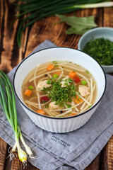 Chicken soup with noodles and vegetables in a white bowl on a rustic wooden background