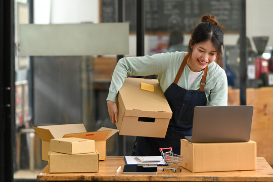 Small business owner in apron using laptop while working at warehouse for online seller