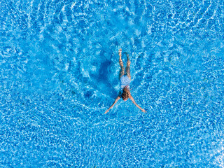 Top view of woman in swimsuit swimming in pool from above view, aerial top view from drone, summer relaxation in hotel