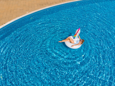 Woman Relaxing In Pool Float Unicorn Inflatable Ring Floating On Turquoise Pool Water. Aerial Top View From Drone