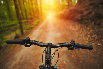 First person view of handling the bicycle on the empty forest road towards sunlight. Outdoor bike riding during sunny summer evening