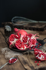 beautiful pomegranate fruits with pits on a metal plate on a wooden table in a dark key in rustic style