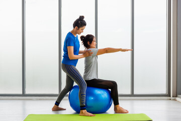 Two Asian adult female and trainer young woman in sportswear doing aerobics yoga exercise with sitting on fitness ball indoor yoga studio, fit sport healthy workout lifestyle exercise