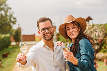Young smiling couple tasting wine at winery vineyard - Friendship and love concept with young people enjoying harvest time 