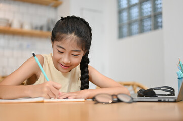Lovely pretty Asian preteen girl doing a homework at desk