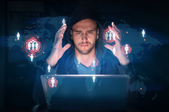 Handsome businessman in hoodie at workplace working with laptop to hire new employees for international business consulting. HR, social media hologram icons over office background