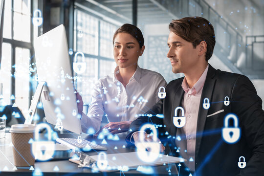 Businessman and businesswoman working together to protect clients confidential information and cyber security. IT hologram padlock icons over office background with panoramic windows.