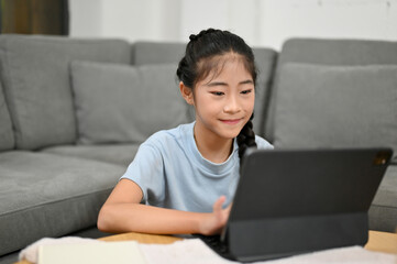 Cute Asian young girl watching something on tablet screen
