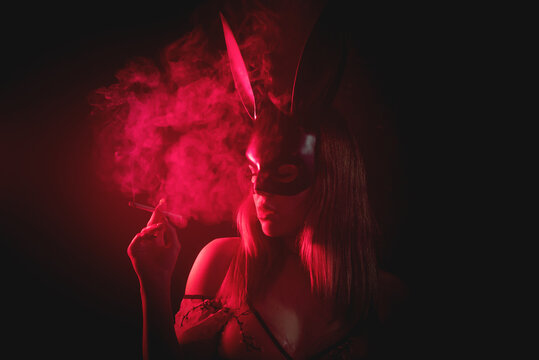 Girl in the rabbit mask in the red light is smoking a cigarette in the dark.