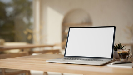 Laptop computer on wooden tabletop over blurred modern minimal cafe in background.