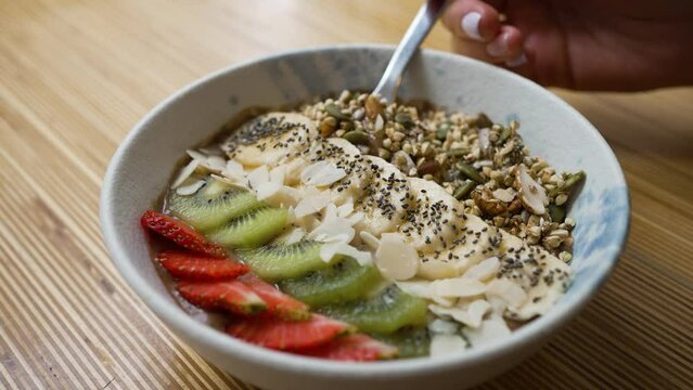 Vegan bowl with banana kiwi and strawberry on wooden table. Cocoa yogurt taken by tablespoon. Vegan bowl with fruits and seeds for breakfast closeup