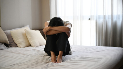 A sad young man sits on bed with arms around his shoulders in bedroom. domestic violence