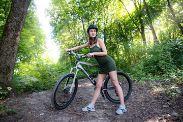 Young sexy active woman in green dress stand near bicycle in the forest