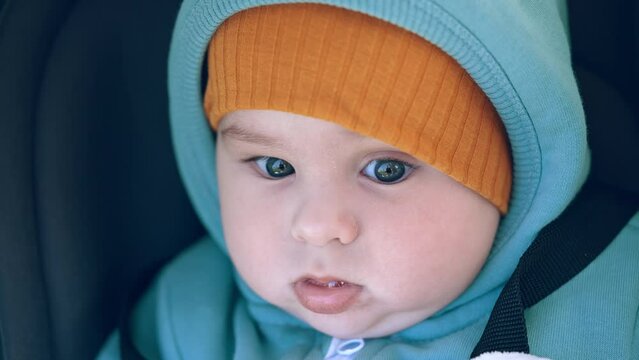Baby in warm clothes at walk. Beautiful peaceful child in cap looking calmly into camera. Close up portrait.
