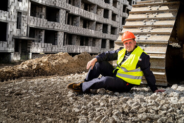 a strong worker in uniform sits on an open ground with a stone grader