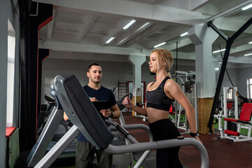 Fit female client running on treadmill with her personal trainer in a sport centre