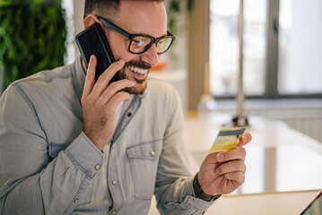 Happy professional talking on cellphone while looking at credit card in office