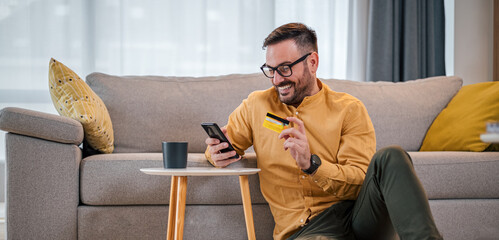 Excited man making online payment with credit card through cellphone at home