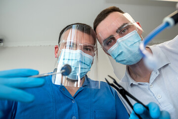 Fototapeta na wymiar Bottom view of male dental doctor and his assistant with stomatological instrument look on patient