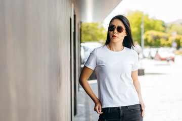 Stylish brunette asian girl wearing white t-shirt and glasses posing against street , urban clothing style. Street photography	
