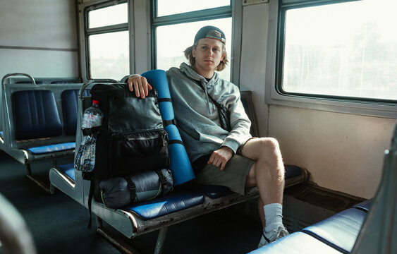 Young male tourist sits in a train in a train with a tourist backpack and goes on a trip.