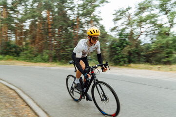 Photo of a professional cyclist riding fast on an asphalt road in the woods.
