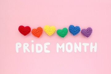 Crochet hearts rainbow colors and Pride Month lettering on pink background. LGBT flag gay pride community, equal rights movement and gender equaluty life concept. Flatlay idea for postcard, poster