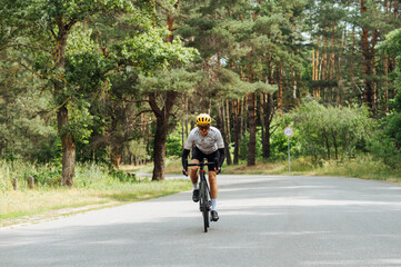 Young man in sports equipment trains in the woods outside the city and rides on an asphalt road.