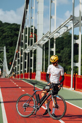 Male professional cyclist in sportswear stands on the street with a bicycle and poses for the camera.
