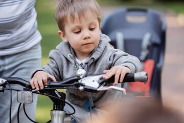 Cute little caucasian boy sitting on frame of father bicycle. Family weekend in countryside