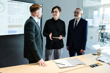 Young businesswoman in eyeglasses with tablet pc discussing new information with her colleague after presentation at boardroom