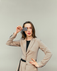 Lady in a beige suit on a beige background with a bank card in hand stands and looks at the camera with a serious face