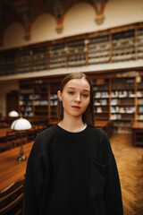 Portrait of a beautiful woman in black clothes in a public library and looking at the camera with a serious face.